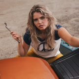Woman holding a wrench next to a car in an outdoor setting 
