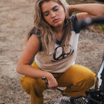 Woman in a sleeveless top and yellow pants sitting on a motorcycle outdoors wearing Soul Sister since 1969.