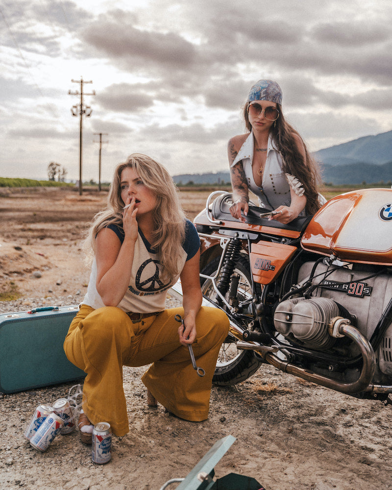 Two women with a motorcycle in an outdoor setting wearing Soul Sister since 1969