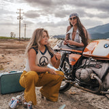 Two women sitting next to a motorcycle in an open area with mountains in the background wearing Soul Sister since 1969.