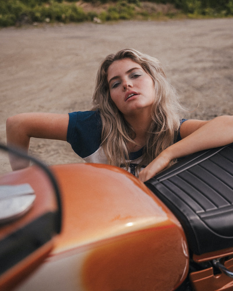 Woman leaning on an orange motorcycle in a desert-like setting 