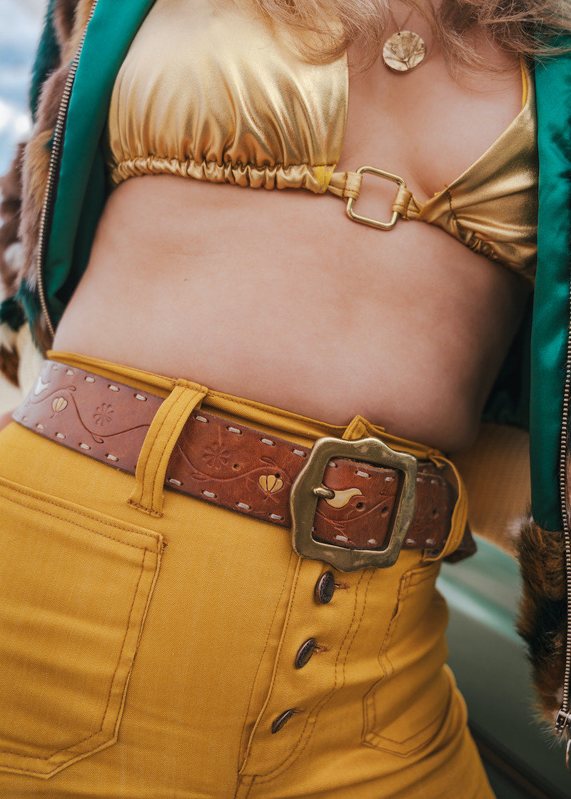 Person wearing a gold top and yellow pants with a brown belt wearing soul sister since 1969.