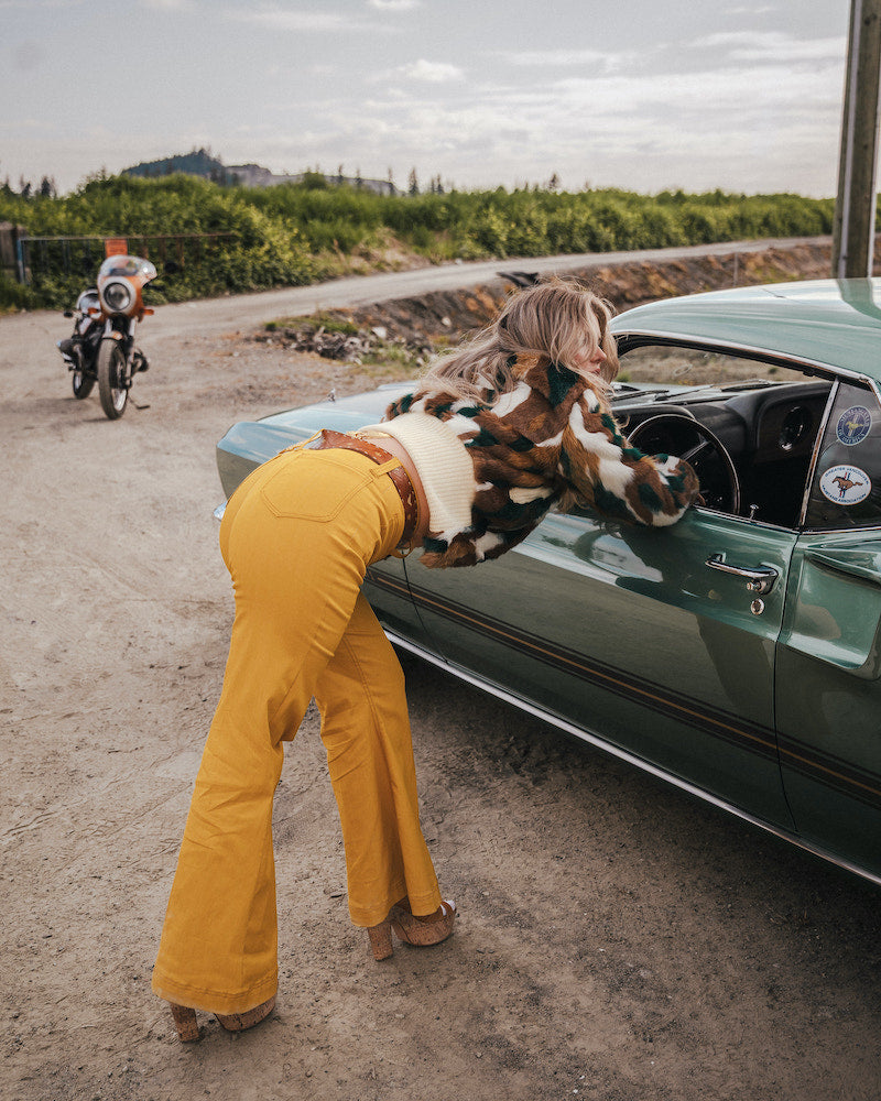 Person in yellow pants with a dog on a car hood, motorcycle in the background wearing soul sister since 1969