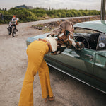 Person in yellow pants with a dog on a car hood, motorcycle in the background wearing soul sister since 1969
