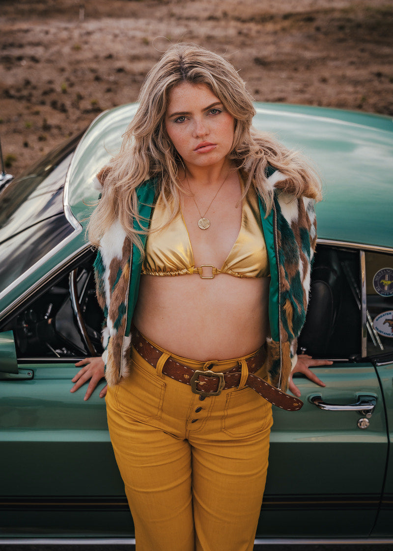Woman in a yellow outfit standing next to a vintage car in a desert setting wearing Soul Sister since 1969