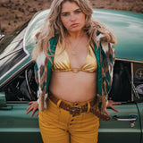 Woman in a yellow outfit standing next to a vintage car in a desert setting wearing Soul Sister since 1969