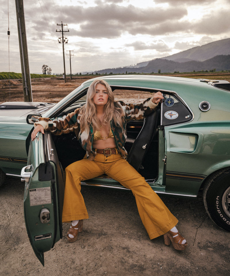 Woman sitting in a vintage car with a scenic background wearing soul sister since 1969
