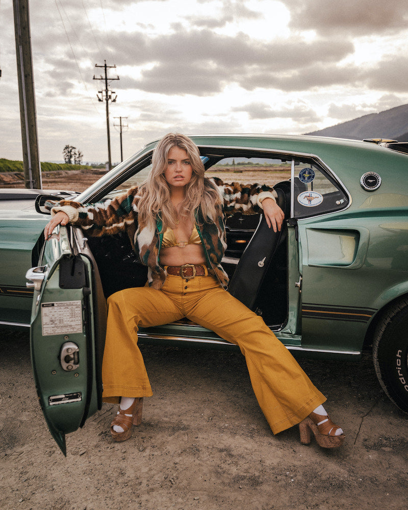 Woman sitting in the door of a vintage car with a desert landscape in the background wearing soul sister since 1969