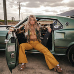Woman sitting in the door of a vintage car with a desert landscape in the background wearing soul sister since 1969