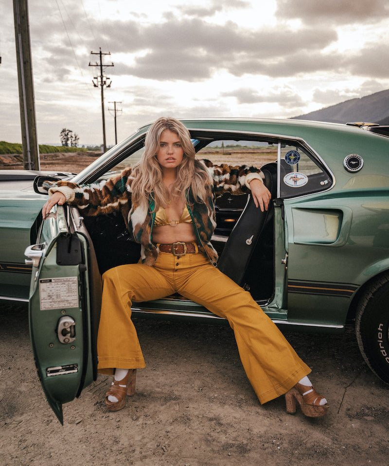 Woman sitting in the door of a vintage car with a desert landscape in the background wearing soul sister since 1969