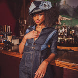 Woman in a denim outfit with a hat standing behind a bar.