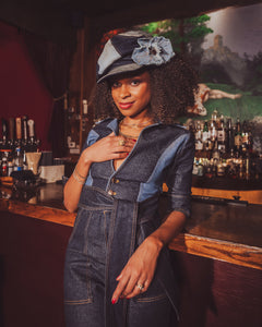 Woman in a denim outfit with a hat standing behind a bar.