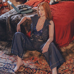 Woman sitting on a patterned rug in a bedroom with a red bedspread and colorful pillows.