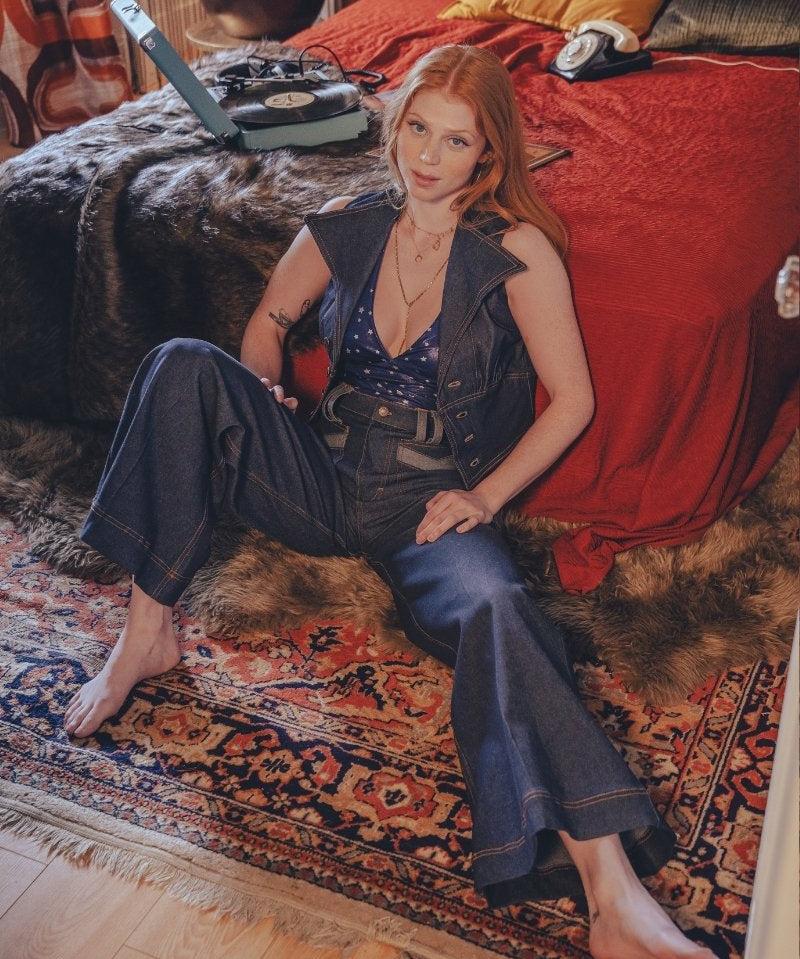 Woman sitting on a patterned rug in a room with a red bedspread and vintage decor.