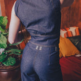 Person wearing a blue denim jumpsuit in a room with a plant and colorful cushions.