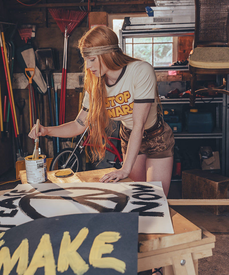 Person painting a peace sign wearing a 'STOP WARS'  tee shirt on it in a workshop.