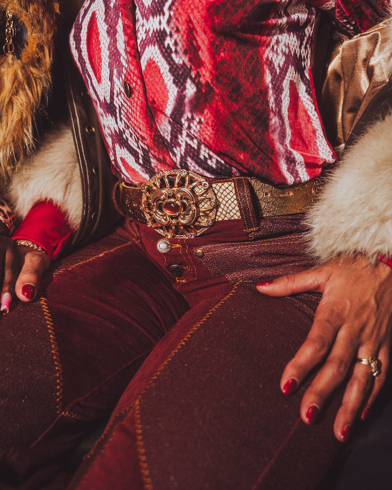 Person wearing a patterned top and red pants with a gold belt, sitting on a textured surface.