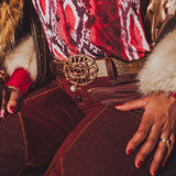 Person wearing a patterned top and red pants with a gold belt, sitting on a textured surface.