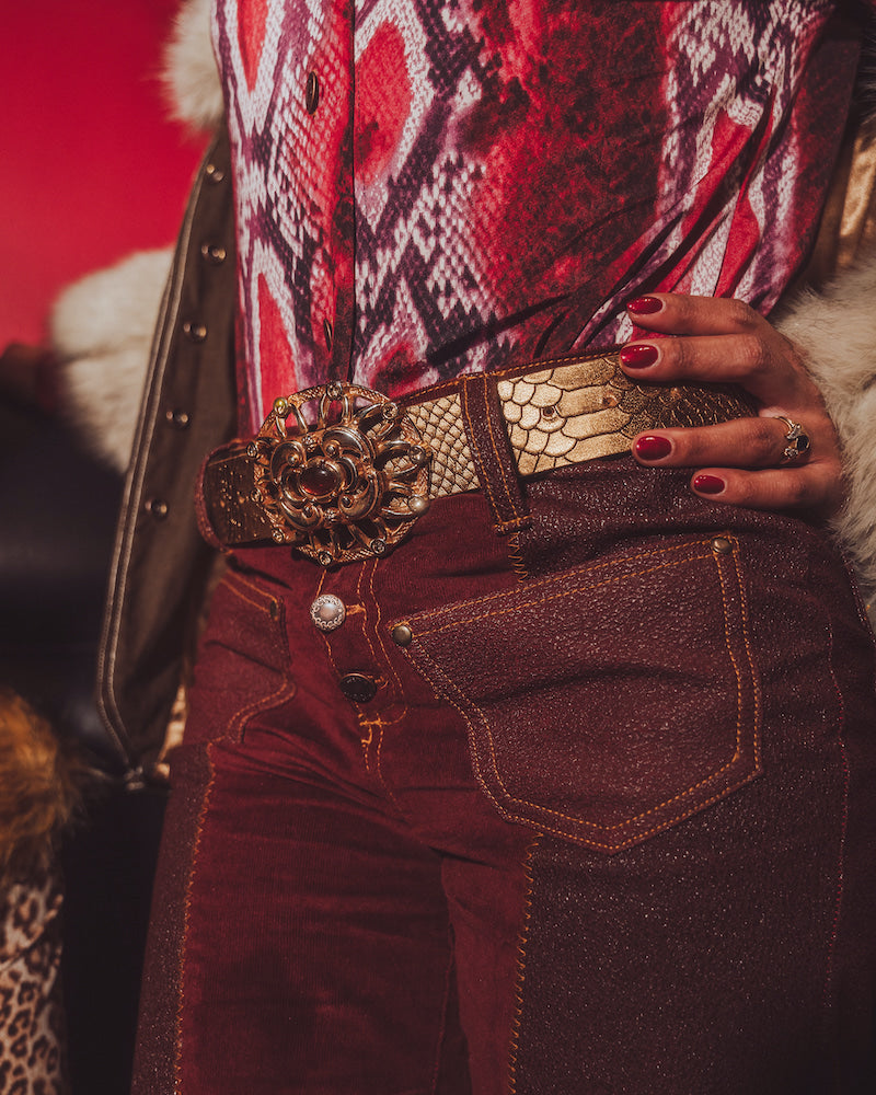 Close-up of a person wearing a patterned top and red pants with a gold belt and clutch.