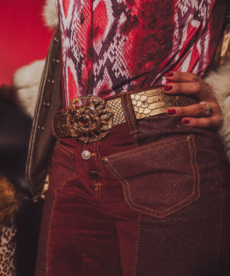 Close-up of a person wearing a patterned top and red pants with a gold belt and clutch.