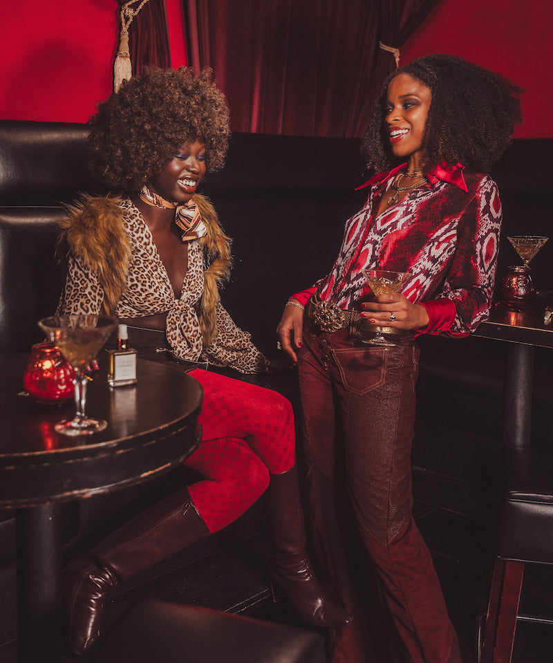 Two women sitting in a stylish bar setting with drinks and decor.