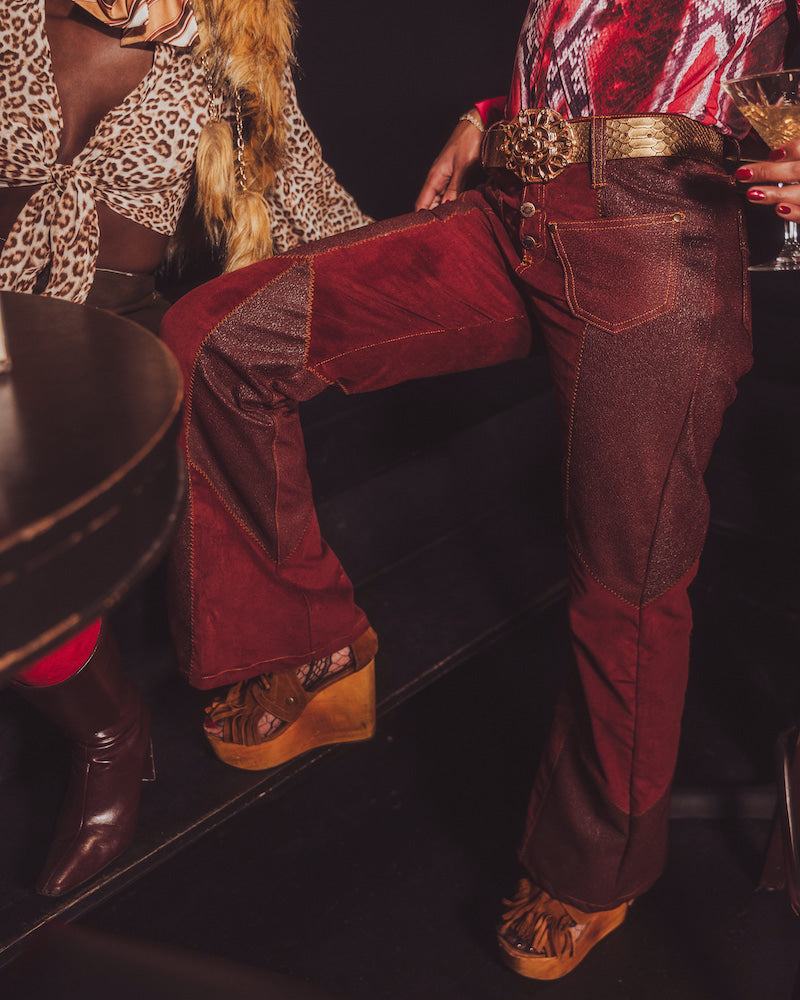 Person wearing red velvet pants and brown boots in a dark setting