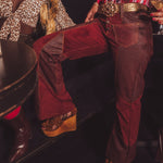 Person wearing red velvet pants and brown boots in a dark setting