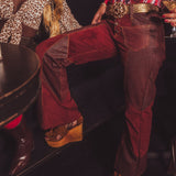 Person wearing red velvet pants and brown boots in a dark setting