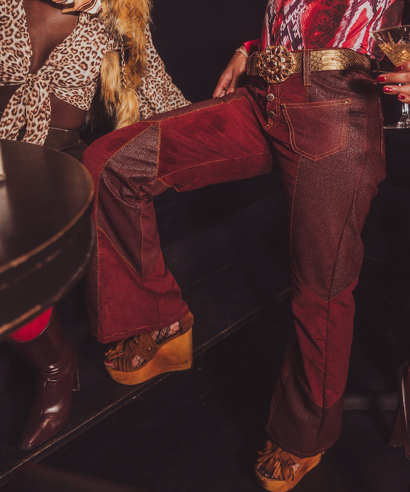 Person wearing red velvet pants and brown boots in a dark setting