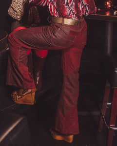 Person wearing a patterned shirt and red pants sitting inside a vehicle.