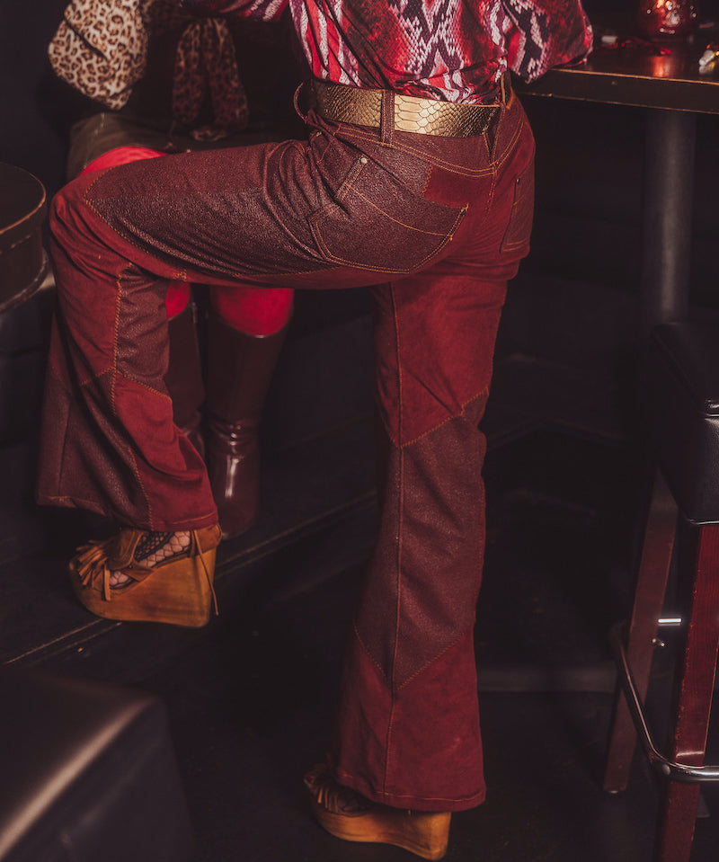 Person wearing a patterned shirt and red pants sitting inside a vehicle.