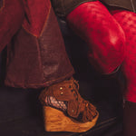 Brown wedge shoe with wooden sole worn by a person in red pants.