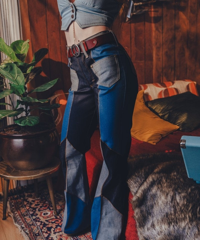 Person wearing a crop top and patchwork jeans in a room with wooden walls and a rug.