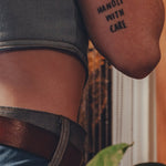 Person wearing a tattoo on their arm with the text 'HANDLE WITH CARE' against a blurred background.