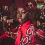 Woman wearing a red hat with a flower and patterned outfit in a bar setting