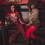 Two women sitting on a couch in a stylish setting with drinks and art in the background.