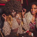 Two women in a social setting with one wearing a leopard print top and fur coat.