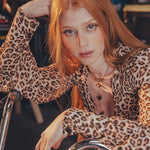 Beautiful redheaded woman sits on a bike wearing a long sleeve leopard print blouse