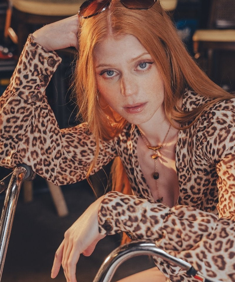 Beautiful redheaded woman sits on a bike wearing a long sleeve leopard print blouse