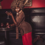 Woman in a brown top and red pants holding a glass in a dimly lit room with a painting on the wall.
