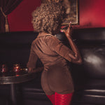 Woman in a brown jacket and red pants taking a photo of a painting in a dimly lit room.