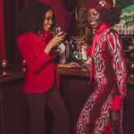 Two women in red and patterned outfits standing in a bar setting.