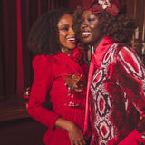 Two women in red and patterned outfits posing together with a drink in a dimly lit setting.