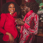 Two women in red and patterned outfits standing close together in a bar setting.