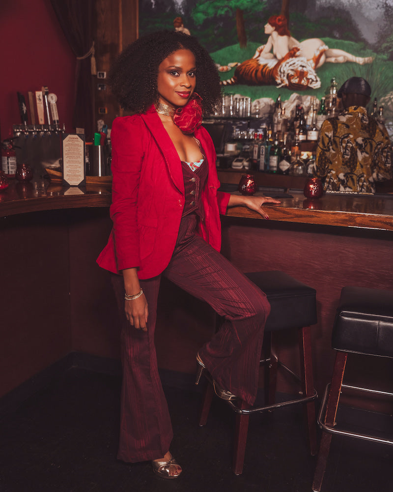 Woman in a red blazer and maroon pants sitting at a bar counter.