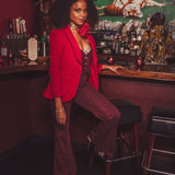 Woman in a red blazer and maroon pants sitting at a bar counter.