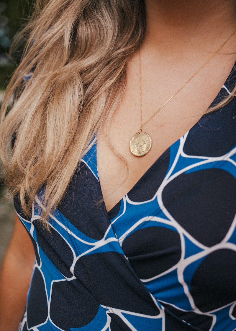 Close-up of a person wearing a blue patterned top with a gold necklace wearing Soul Sister since 1969..