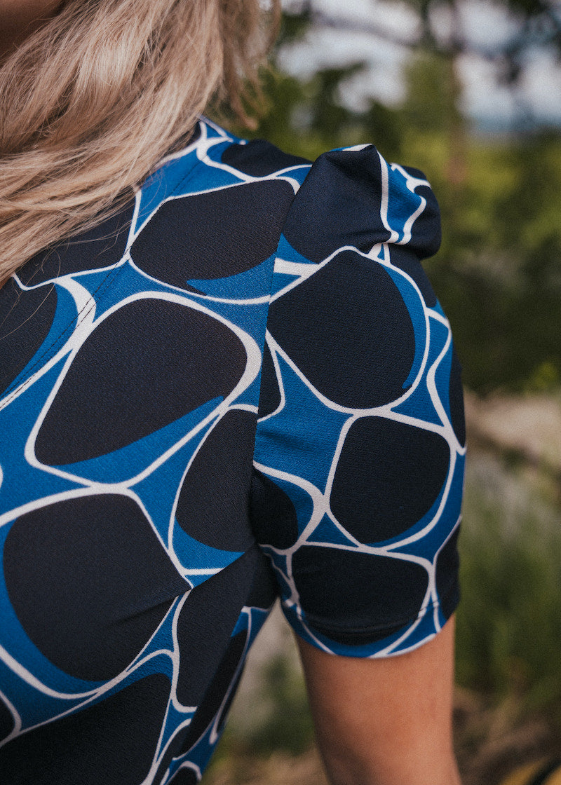 Person wearing a blue and black patterned top with blurred natural background wearing Soul Sister since 1969.