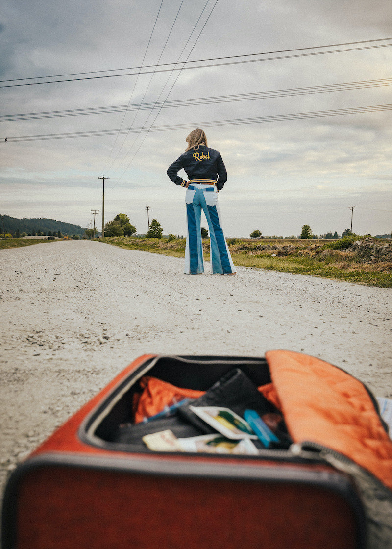 Person standing on a road with an open suitcase in the foreground wearing Soul Sister since 1969