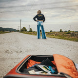Person standing on a road with an open suitcase in the foreground wearing Soul Sister since 1969